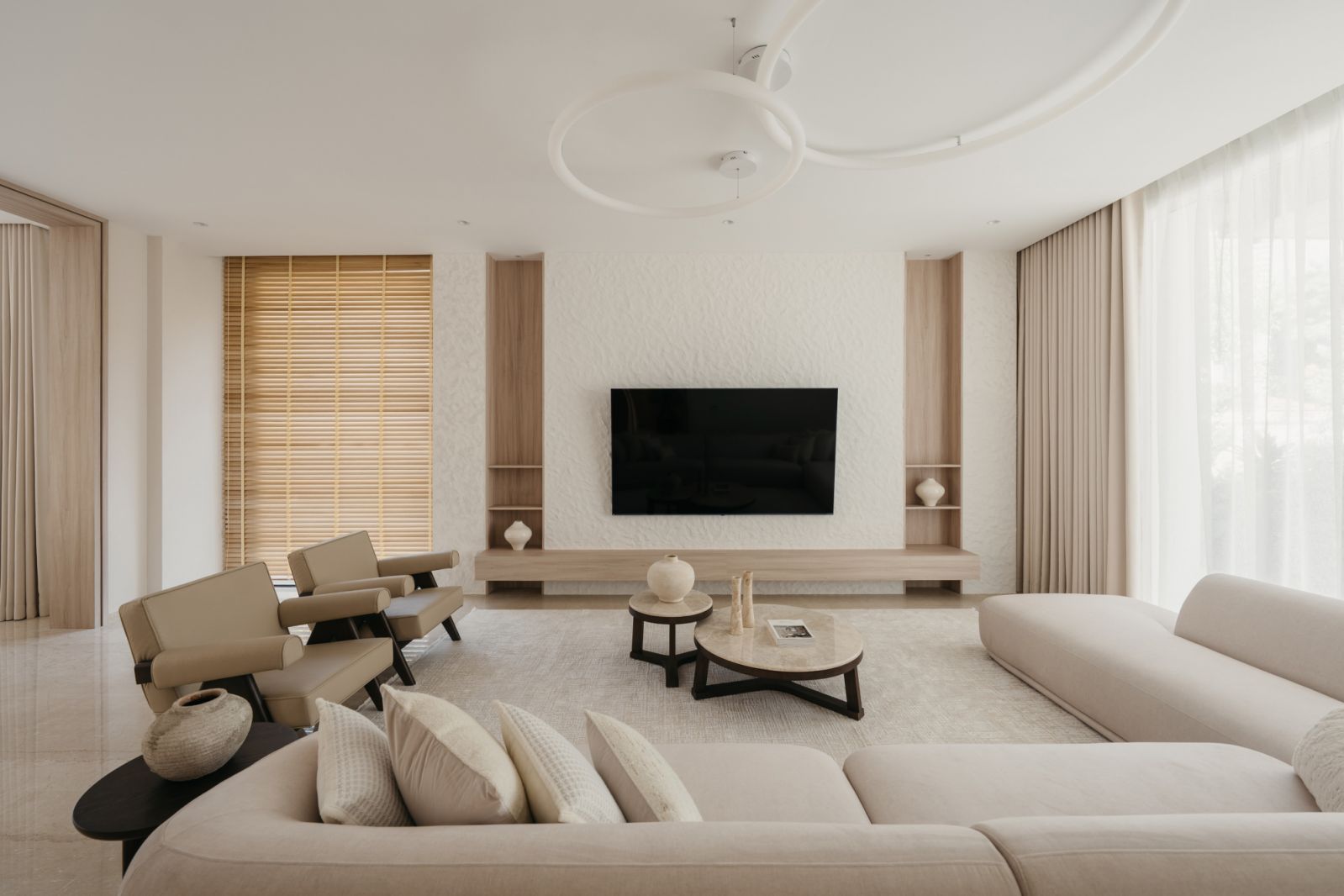 The living room features curved modular seating, bespoke wooden shelving and a textured white accent wall