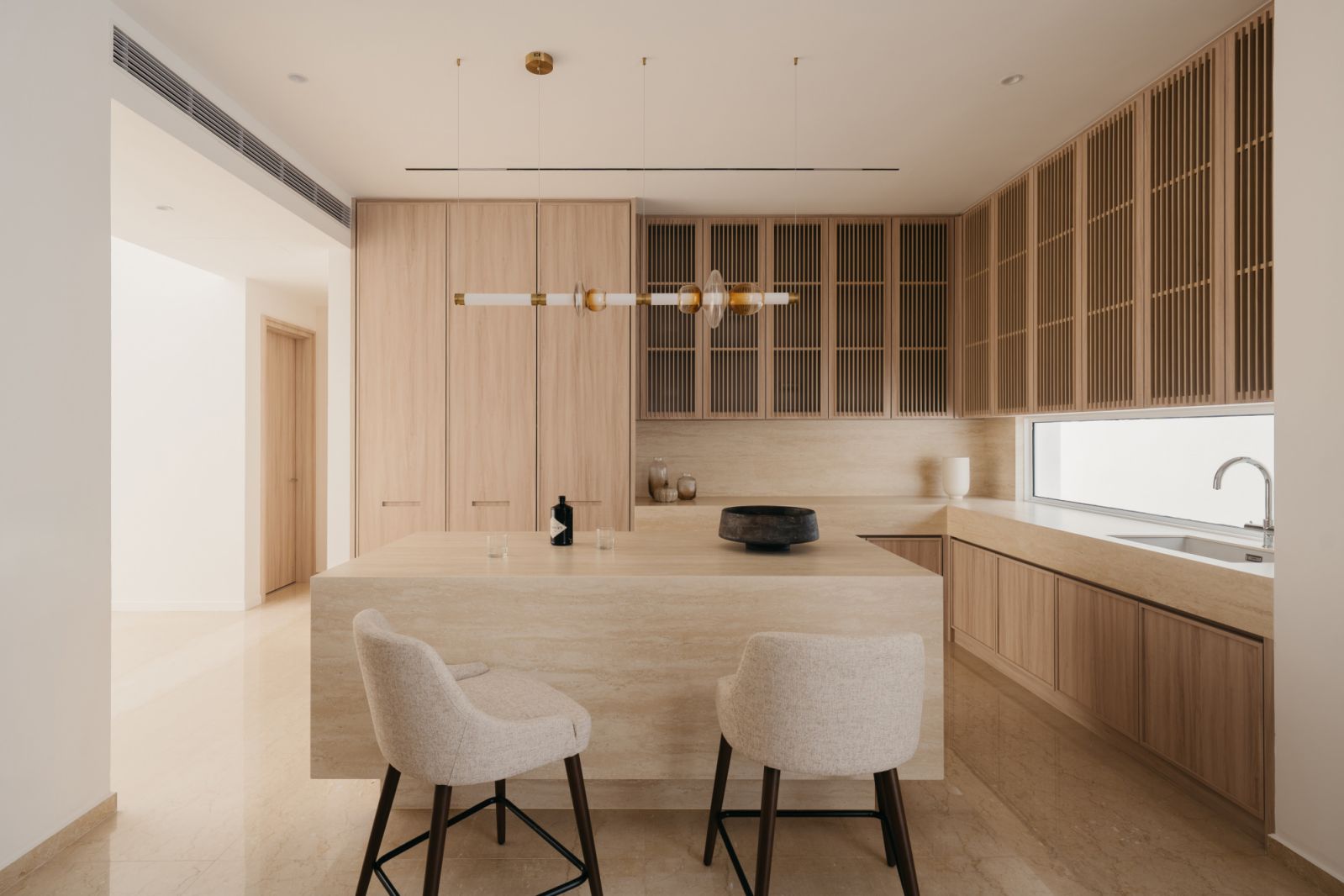 Monolithic limestone island with integrated sink complements pale oak cabinetry in this minimalist kitchen