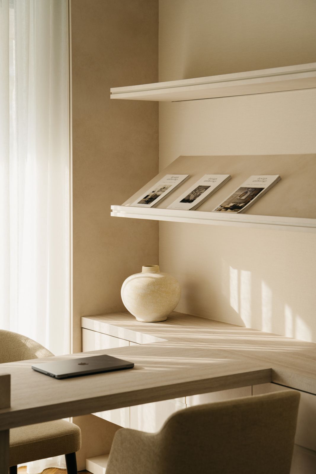 Minimalist home office corner with floating shelves, ceramic vessel and natural light optimizing the neutral palette.