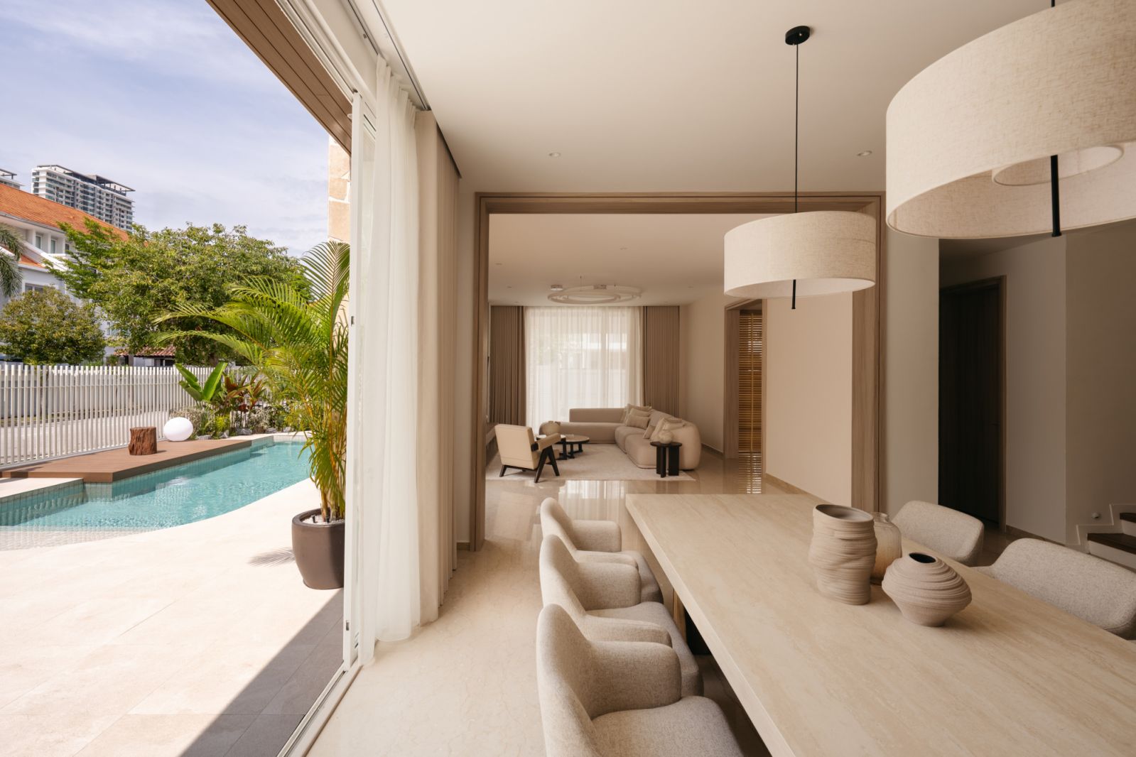 Open-plan dining area with limestone table flowing to outdoor spaces through full-height sliding glass doors