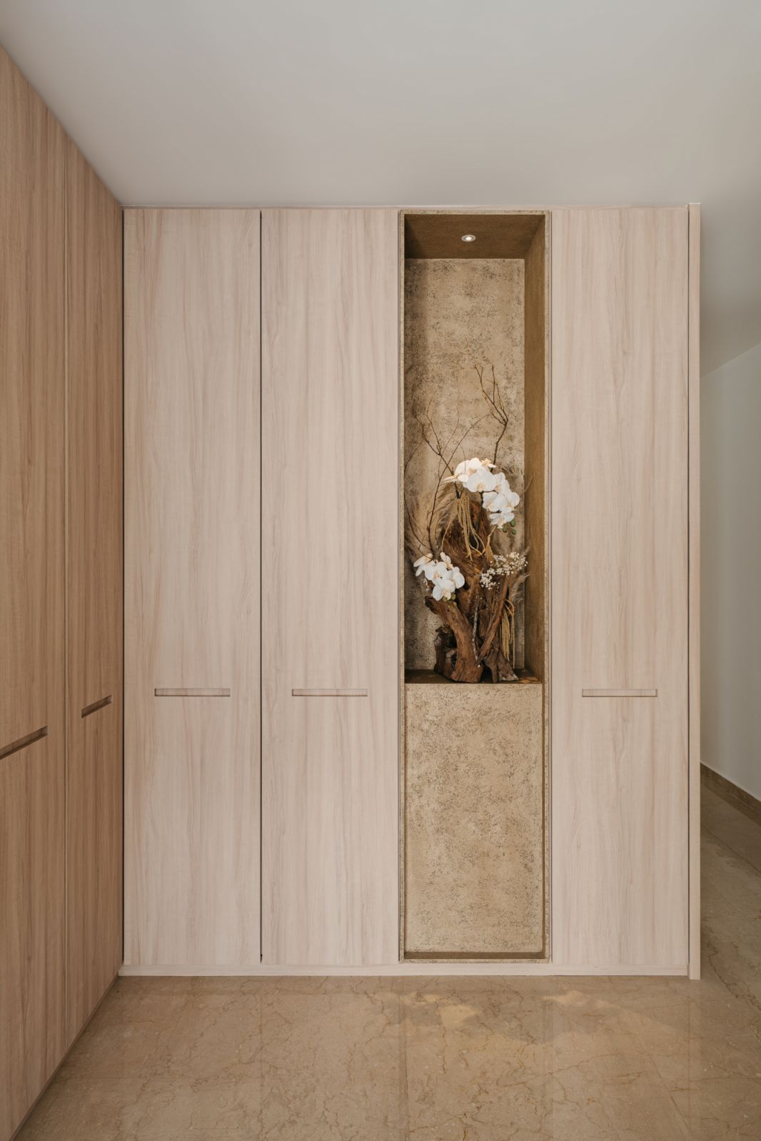 Bleached wood wardrobe with recessed handles and limestone-lined display niche showcasing dried floral arrangement in master suite entryway