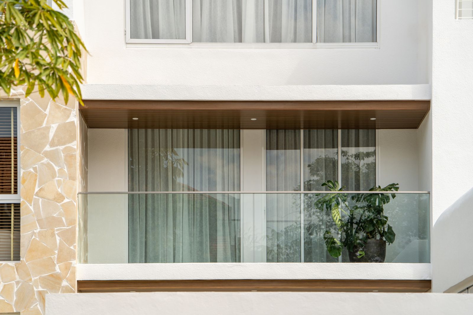 Striking limestone-clad facade with resort-style balcony featuring tropical plants