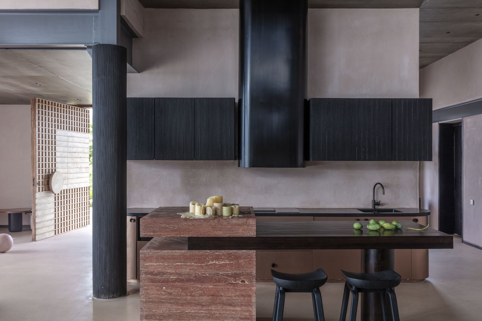 The kitchen in a summer home in Hyderabad, India, pairing red travertine and black-stained wood for the island with densely fluted black cabinetry behind