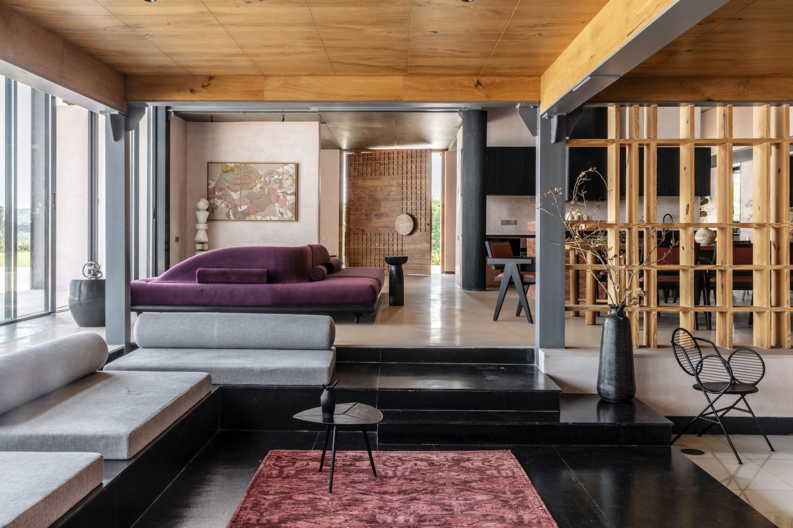 The living room and sunken television area of a Hyderabad, India home and contrasts muted jewel tones with natural materials