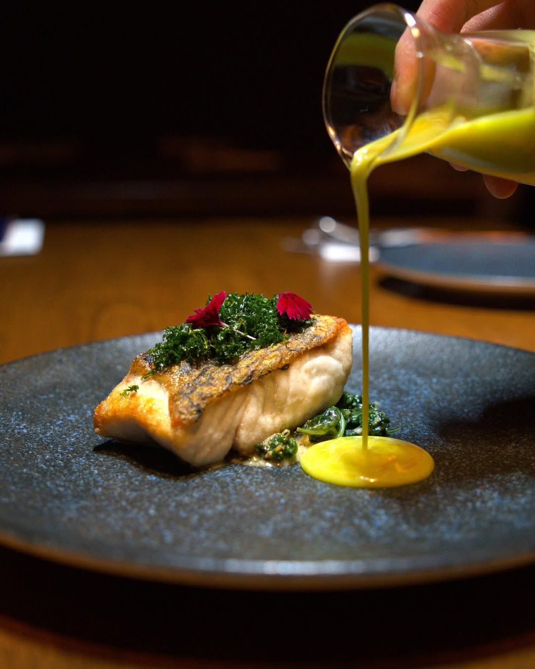 Golden-crisp siakap served with a sautéed bayam and umami rich dried shrimps. A touch of chili tinctures add a subtle heat, balanced by a silky parsley-lemon beurre blanc for a bright, herbaceous finish. (Image: @theriffdistrict)