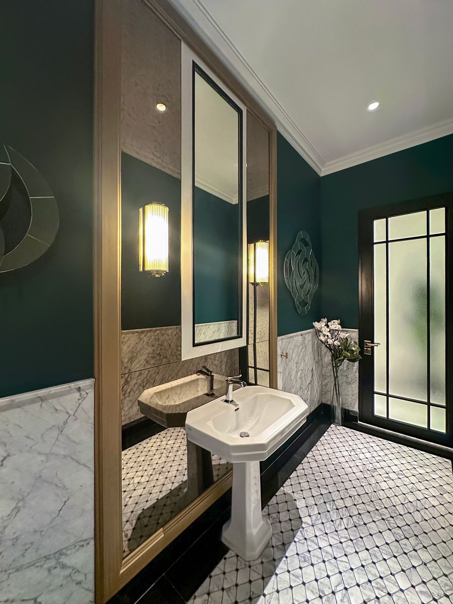 The powder room’s black-and-white material palette is given a lift with a deep green hue