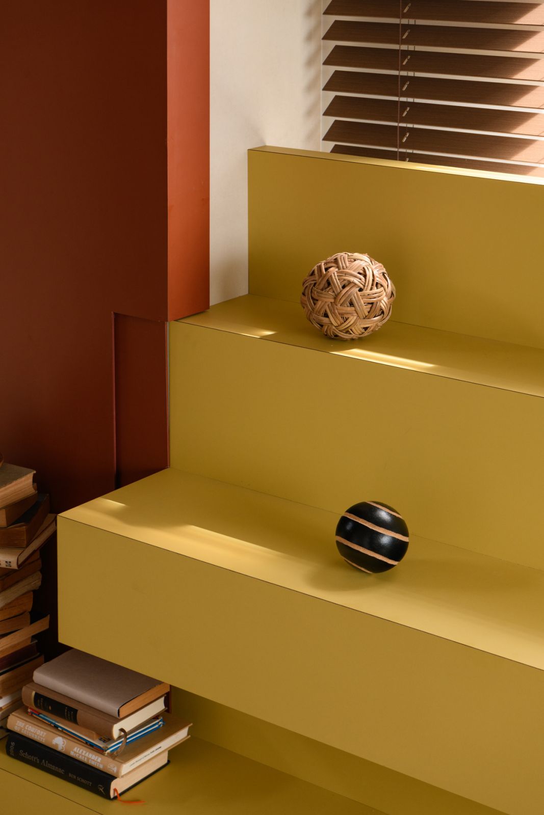 Bold yellow shelving creates a playful focal point against terracotta and cream tones, showcasing the designers’ strategic use of colour to define zones within the open plan space