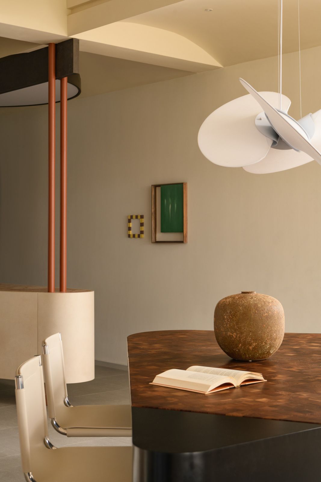 The sculptural dining area features a rich wooden table and contemporary seating beneath an innovative orbital pendant light