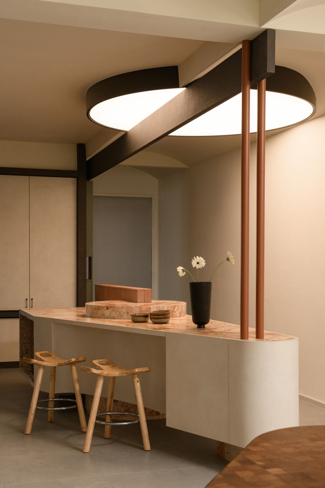The innovative orbital light fixture crowns the curved kitchen island, forming a dramatic focal point that softens the kitchen’s angular geometry.