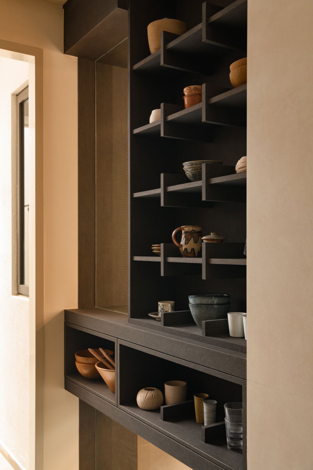 Custom dark shelving showcases the ceramic artist homeowner’s collection of handcrafted vessels in this Puchong terrace house