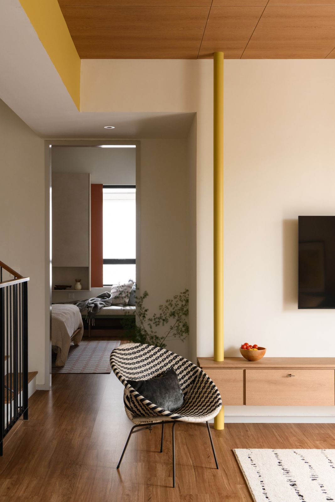 Strategic yellow accents create visual connectivity throughout this quirky Malaysian terrace house, where a pattern-woven chair creates an inviting transition point between bedroom and hallway