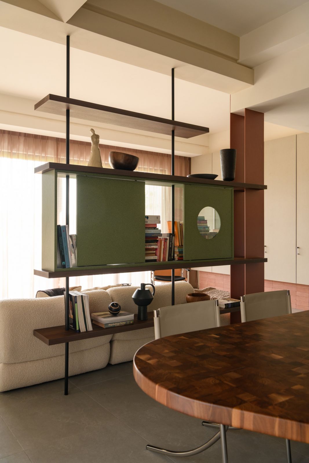 The custom floating bookshelf with green panels serves as both a room divider and a display unit, allowing glimpses between spaces while maintaining distinct zones.