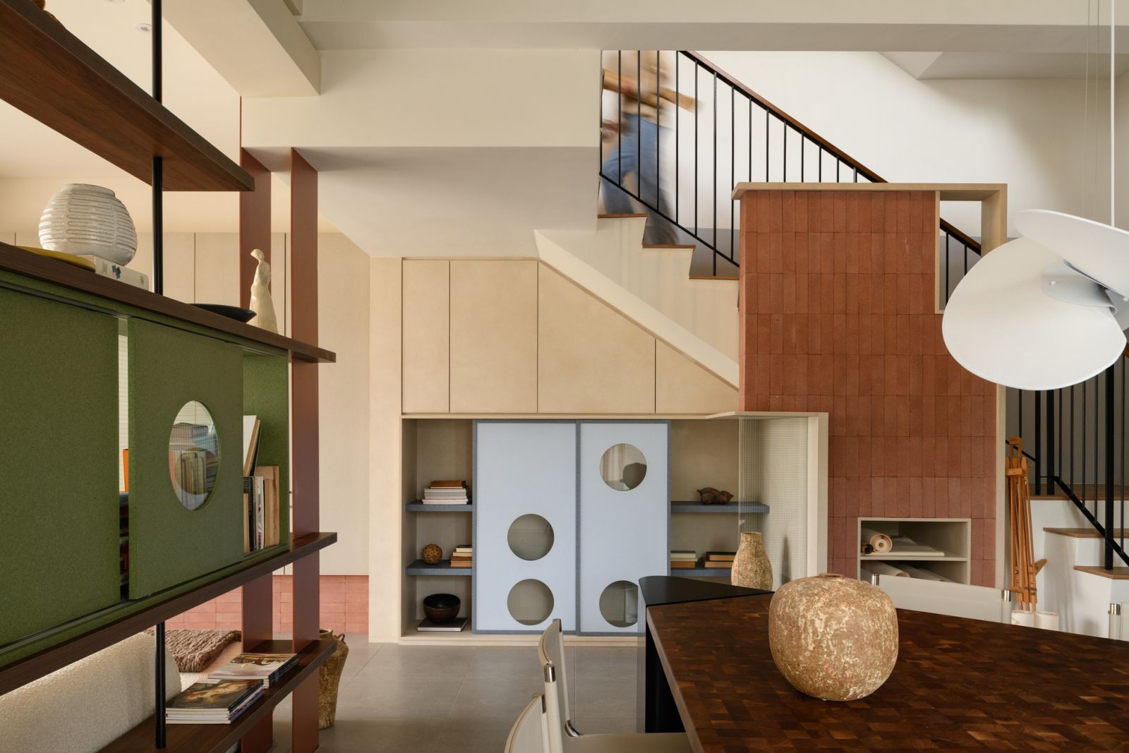 The carefully designed staircase incorporates storage solutions beneath, while the terracotta wall treatment adds visual warmth and texture