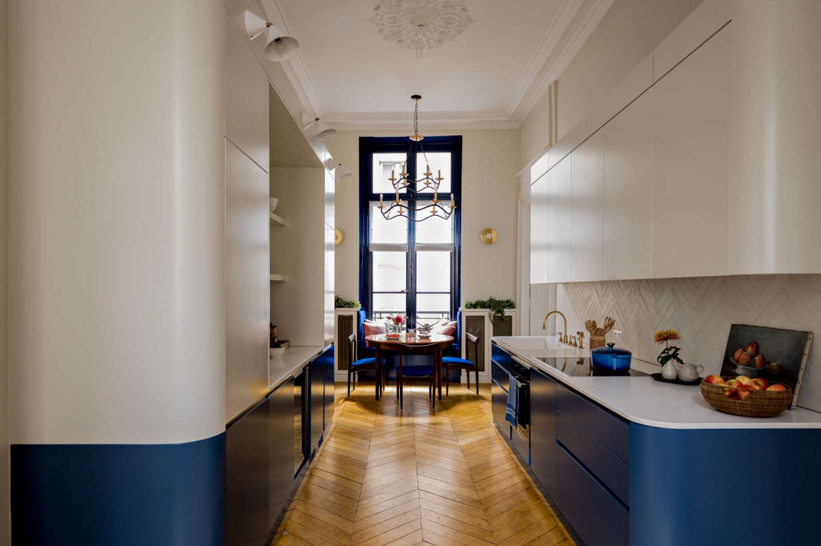 The blue-toned kitchen area with wooden herringbone-patterned flooring and white cabinetry