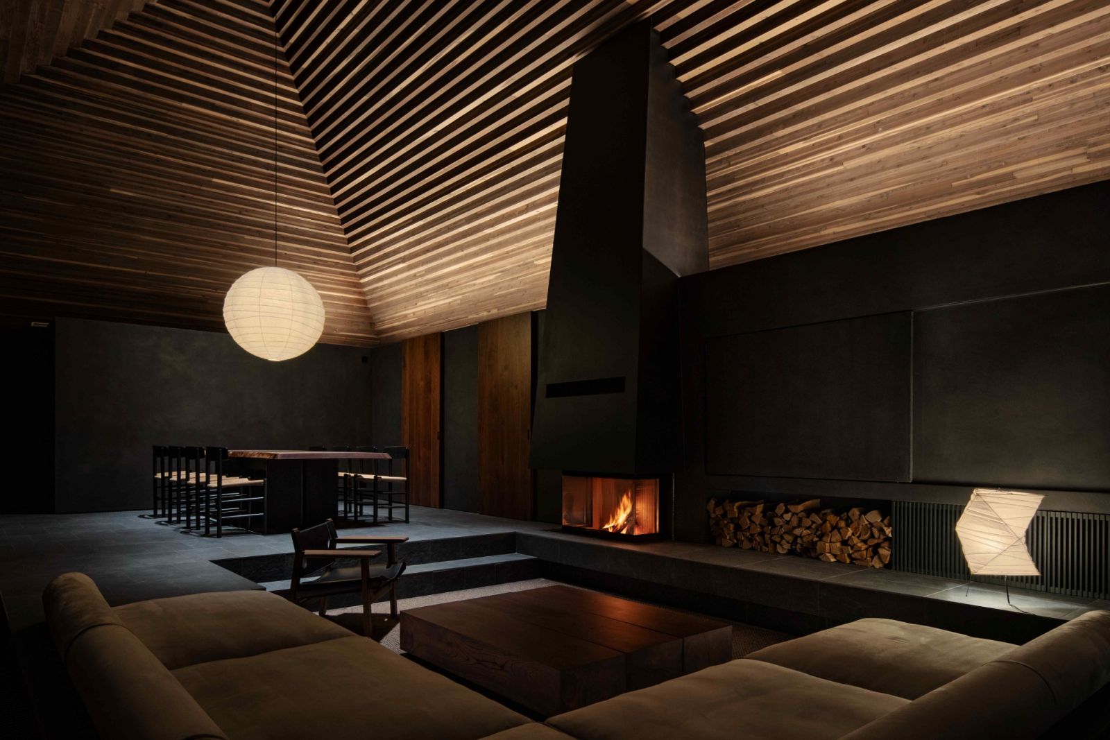 The living area with a six-metre ceiling, a wood stove, and Noguchi’s Akari lamps casting a soft glow