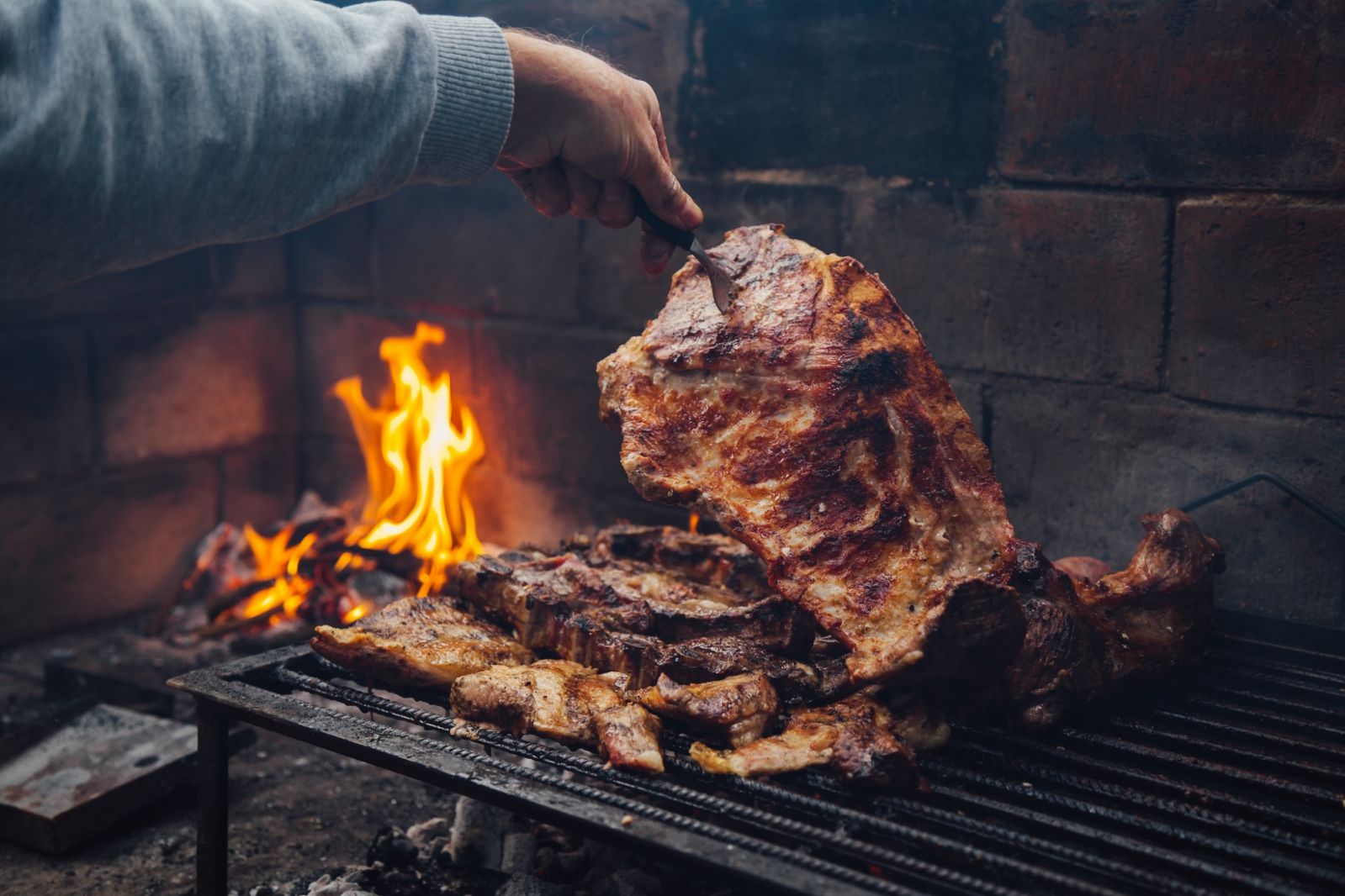 Mature man doing a bbq. He is prodding the meat with a fork. Traditional barbecue called Asado in Argentina.