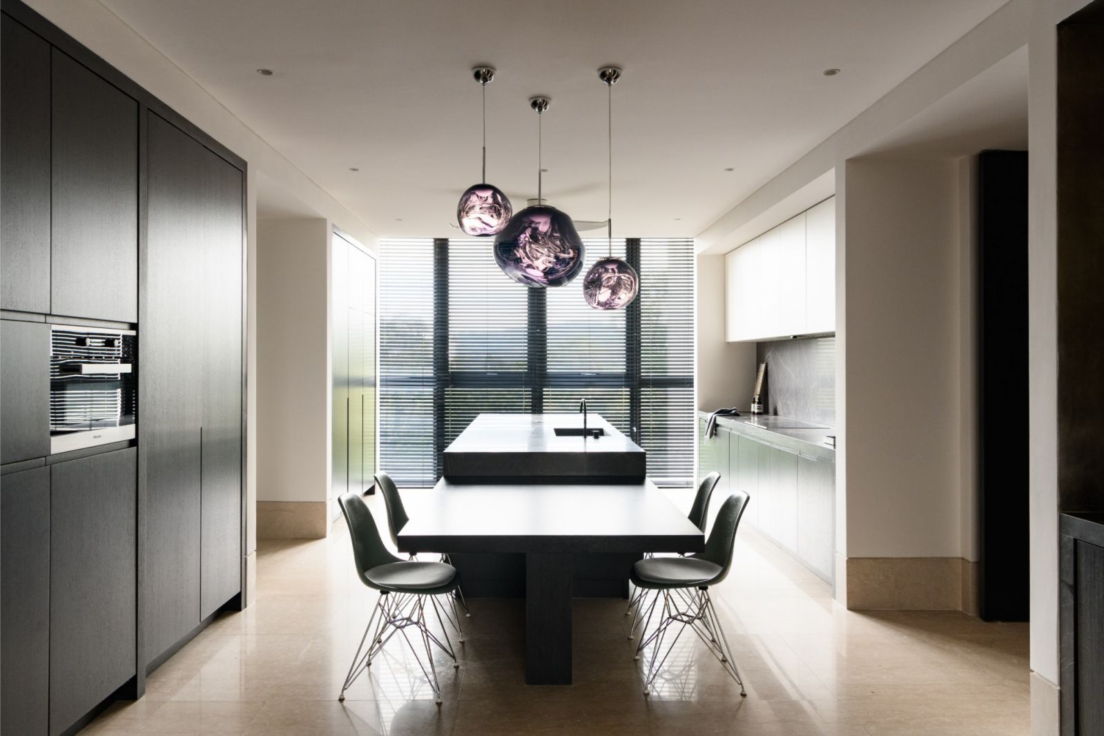 Monochromatic kitchen design featuring purple hand-blown pendant lights above a black dining table with mint green Eames-style chairs