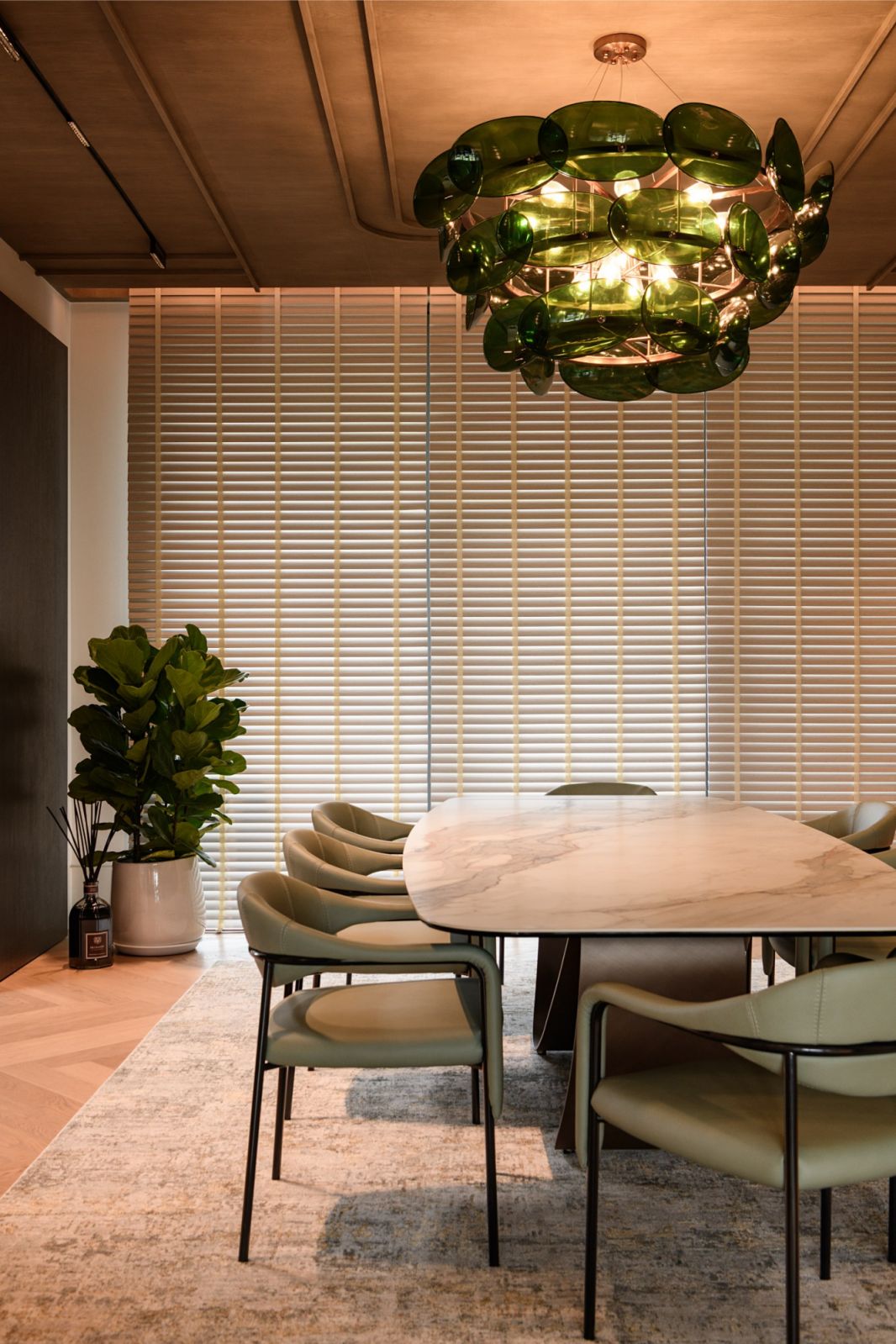 Sophisticated dining space with marble table, sage green chairs and signature teal green hand-blown glass chandelier