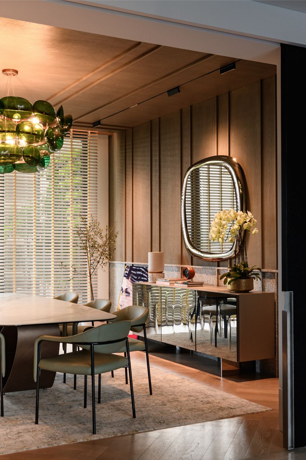 Elegant dining area with textured wood panelling, oval mirror and custom green glass pendant lighting in the Damansara Heights luxury penthouse