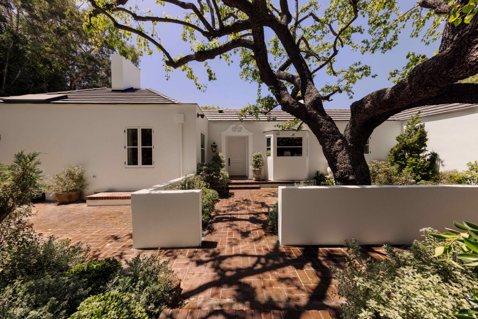 An old towering tree provides ample shade for the California-colonial style residence