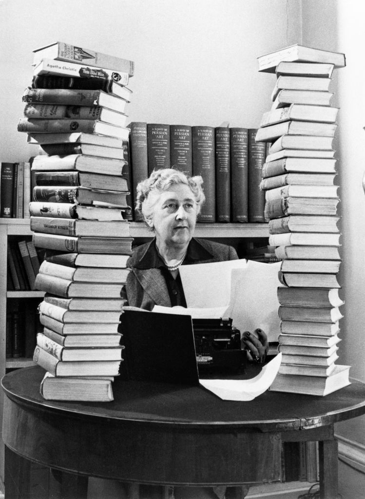 ราชินีอาชญนิยายชาวอังกฤษ Agatha Christie (1890-1976) นั่งอยู่ที่โต๊ะทำงานพร้อมเครื่องพิมพ์ดีดและกองหนังสือปกแข็ง ในห้องสมุดที่บ้าน Winterbrook House ในเมือง Oxfordshire เมื่อปี 1950 เธอเขียนนวนิยายอาชญากรรมและเรื่องสั้นหลายเรื่องที่มีตัวละครหลักเป็นนักสืบในจินตนาการอย่าง “เฮอร์คูล ปัวโรต์” และ “มิสมาร์เปิล” (ภาพ: Jack Esten/Popperfoto via Getty Images)