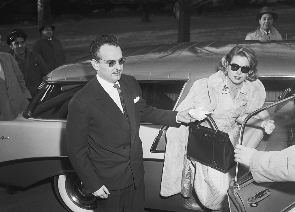 Prince Rainier III of Monaco helping his fiancee Grace Kelly out of a car. Kelly holds the style of Hermes handbag that was named after her.