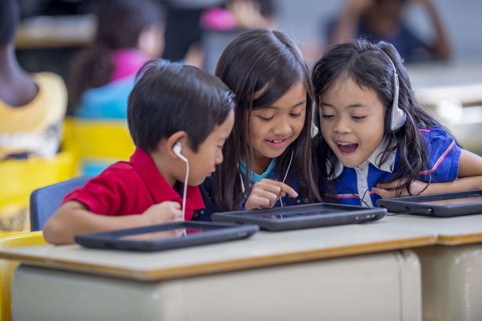 A small group of elementary students sit at a desk as they work aw ay on tablets together during a computer lab. They are each dressed casually and are focused on the screens.