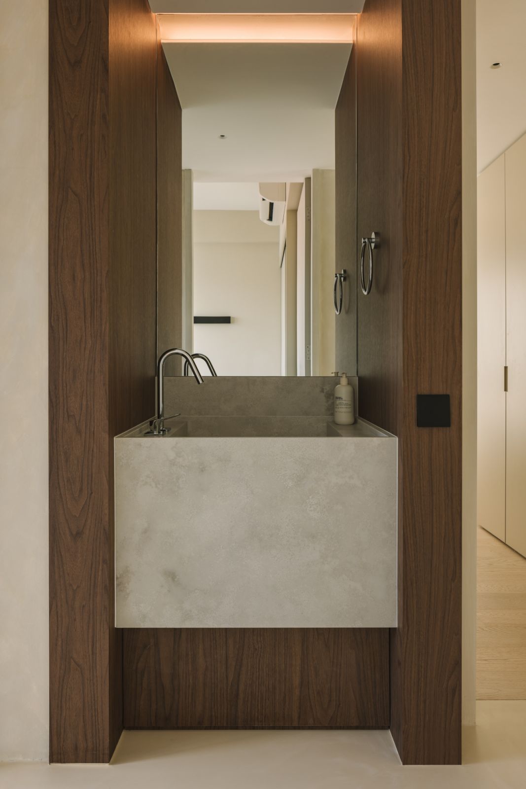 Carved into the corridor wall, this bespoke vanity marries warm wood accents with raw-textured stone; a subtle strip of cove lighting enhances the architectural frame of the basin area, adding warmth and definition to the tactile material palette