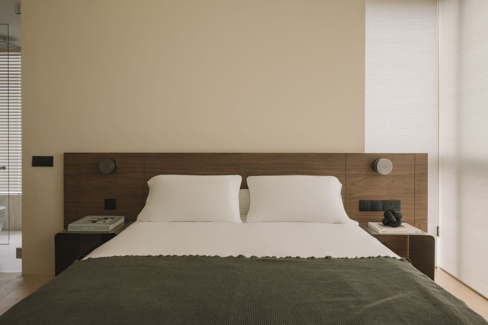 The headboard’s walnut veneer and integrated bedside lights frame the bed in understated elegance, echoing the home’s overall tone of organic calm