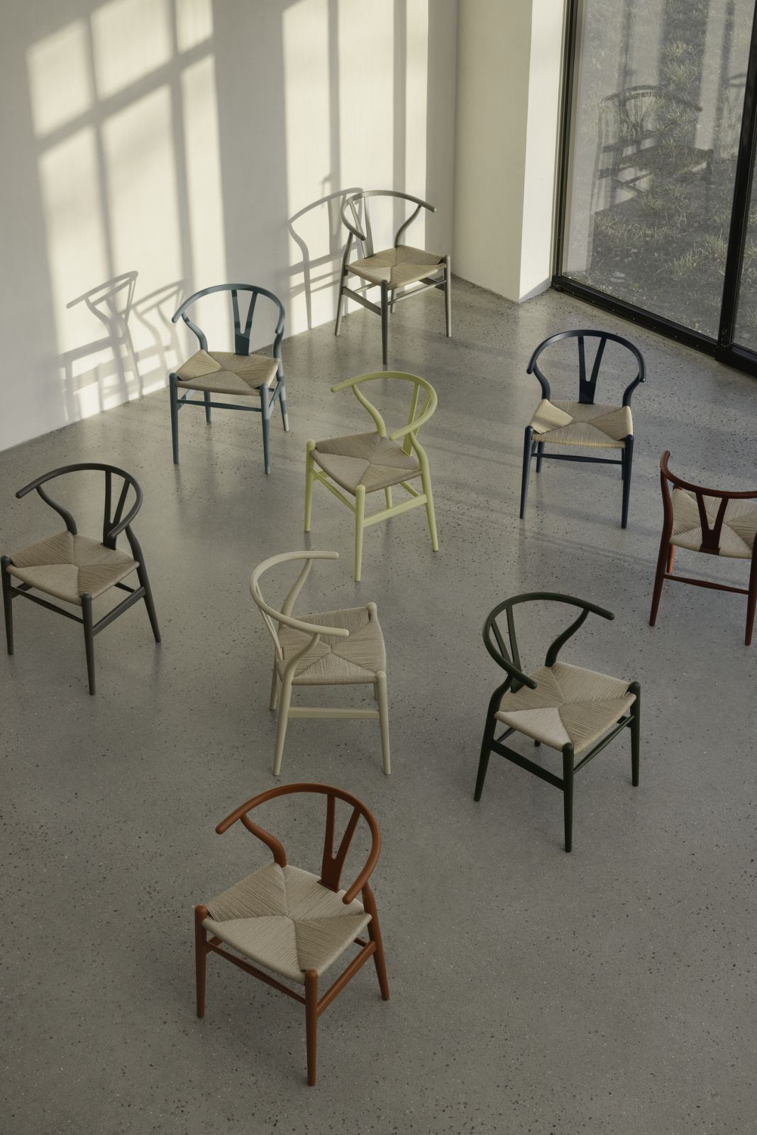 A striking collection of Wishbone chairs is displayed in various finishes—from classic natural oak to contemporary colored frames in sage green, navy, and burgundy (Photo: Carl Hansen & Søn)