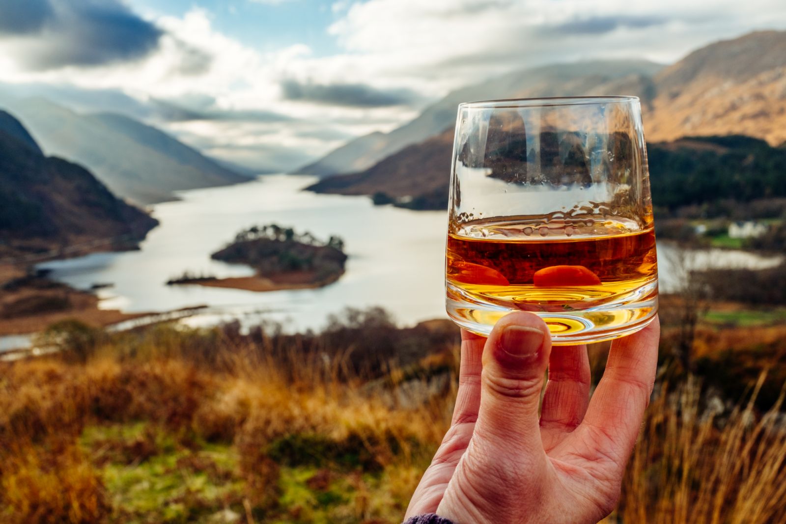 Woman holding a glass of single malt Scotch Whisky above Glenfinnan in the West Highlands of Scotland.