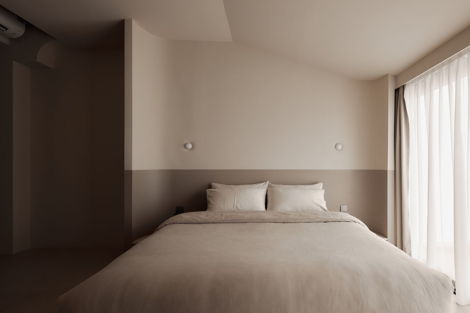 A half-height painted wall anchors the bed while reinforcing the symmetry and softness of the overall scheme
