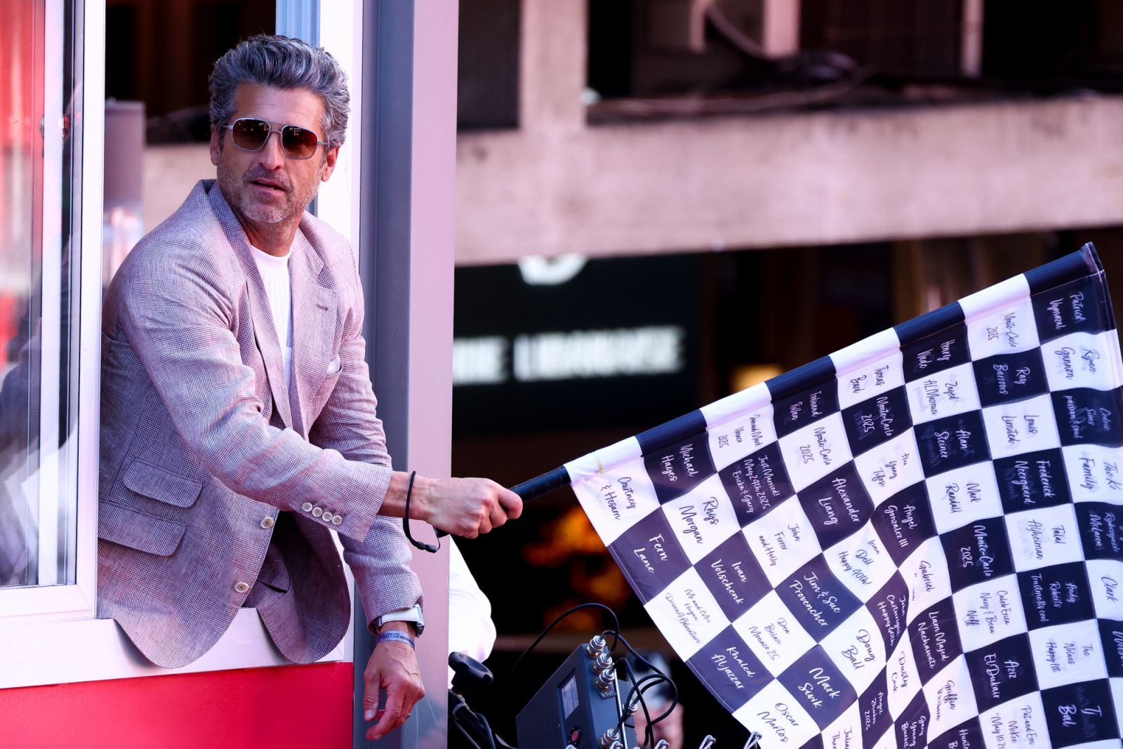 Patrick Dempsey wears a grey blazer while waving the chequered flag during the F1 Grand Prix Of Monaco (Photo by Marc Piasecki/WireImage via Getty Images)