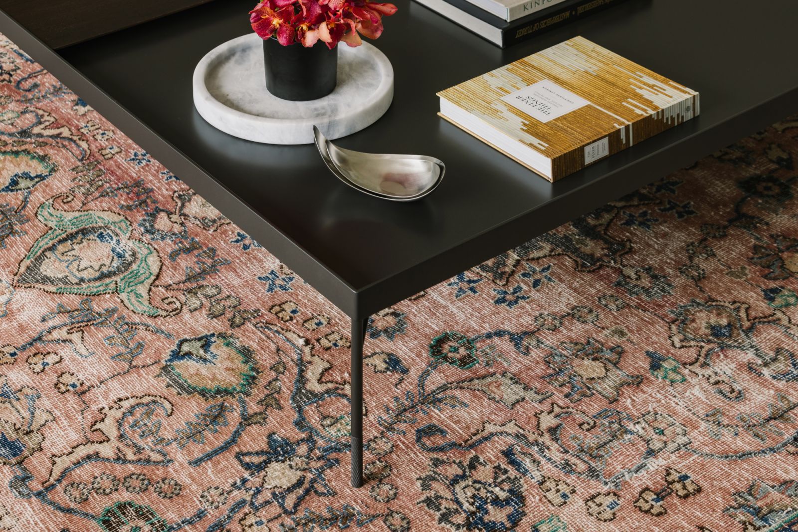 The worn patina of a hand-knotted rug in dusky rose and indigo tones adds depth and warmth—infusing the space with lived-in charm and textural soul