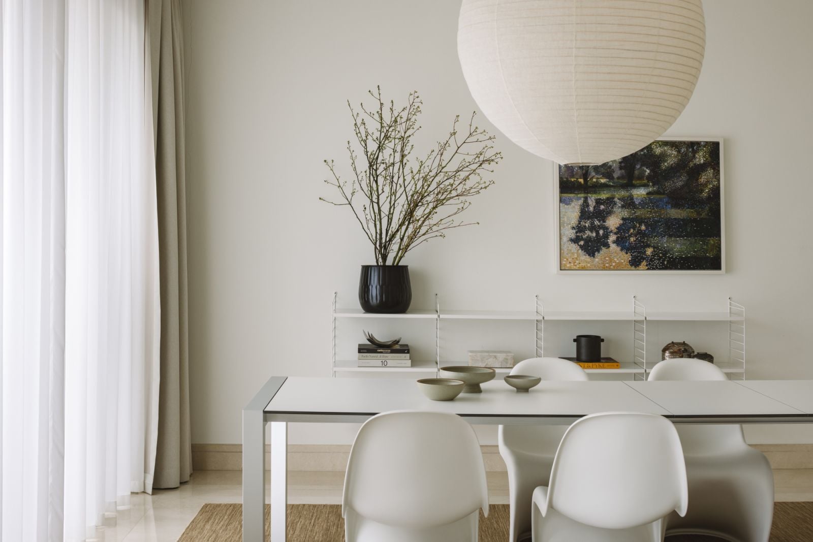 In the dining area, sinuous white chairs and a minimalist table set the stage for slow living, backdropped by open shelving and contemplative art