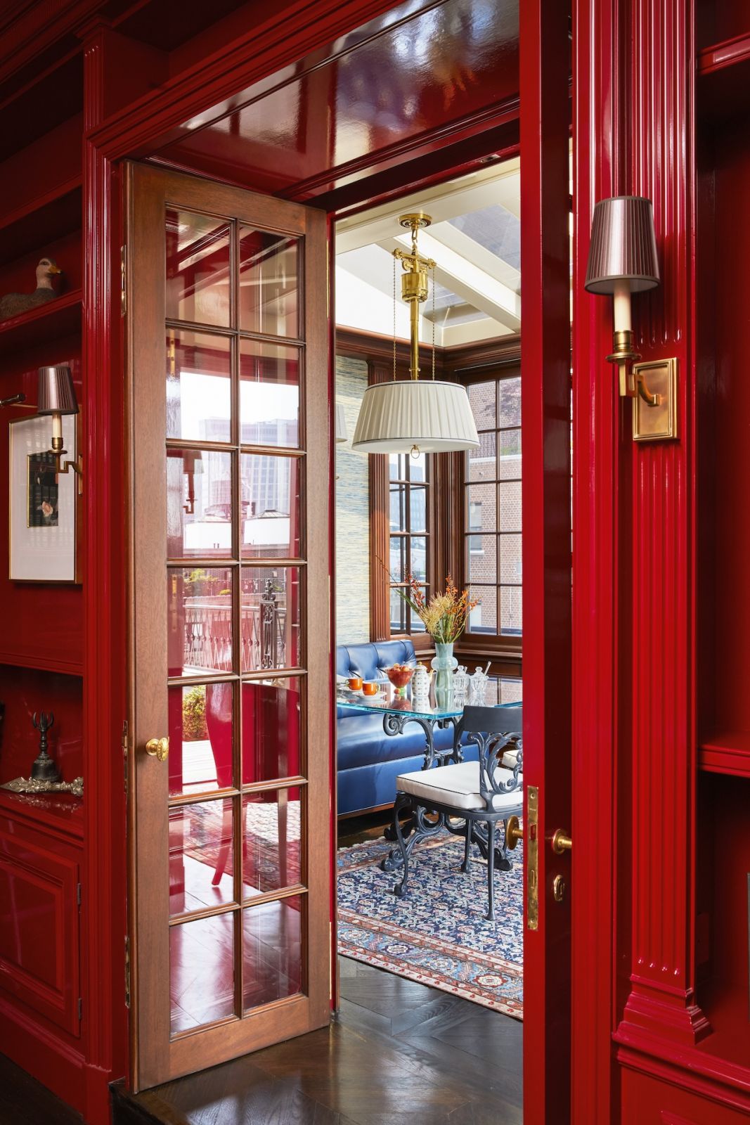 A glimpse of the living room through the vivid red dining room doors at a home on Park Avenue, New York, designed by Phillip Thomas