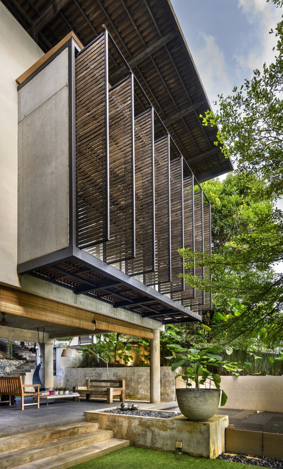 The timber screening system at Denai House exemplifies Razin's passive cooling strategies, providing solar protection while maintaining natural airflow—a contemporary interpretation of traditional tropical design principles.