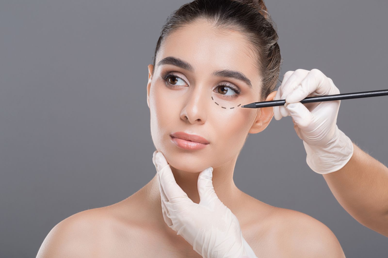Surgeon drawing marks on female face against gray background. Plastic surgery concept