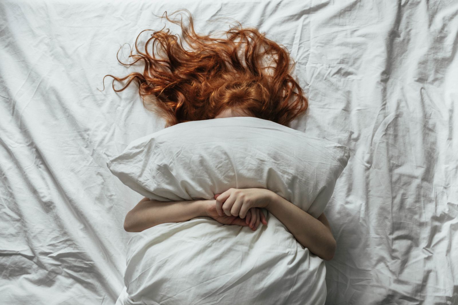 Red-haired little girl wakes up in the morning in her crib with white bed linen.