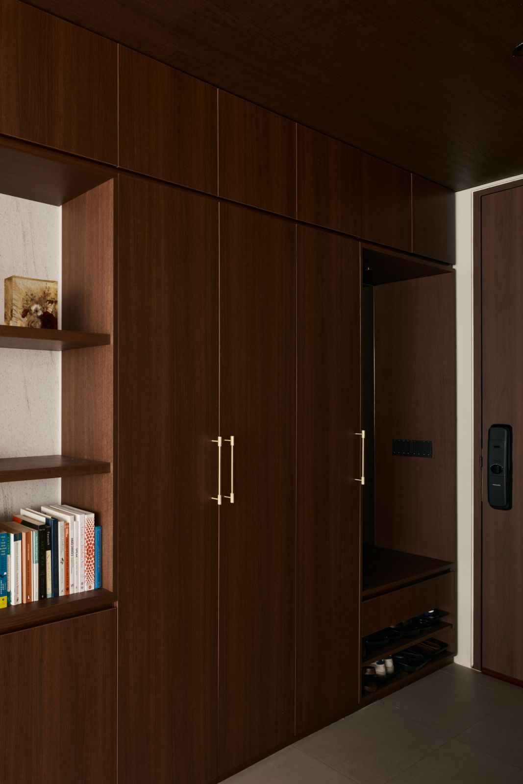 Custom cabinetry in warm wood tones conceals ample storage and integrates seamlessly with the bookshelf—enhancing order and ease of use in the entryway