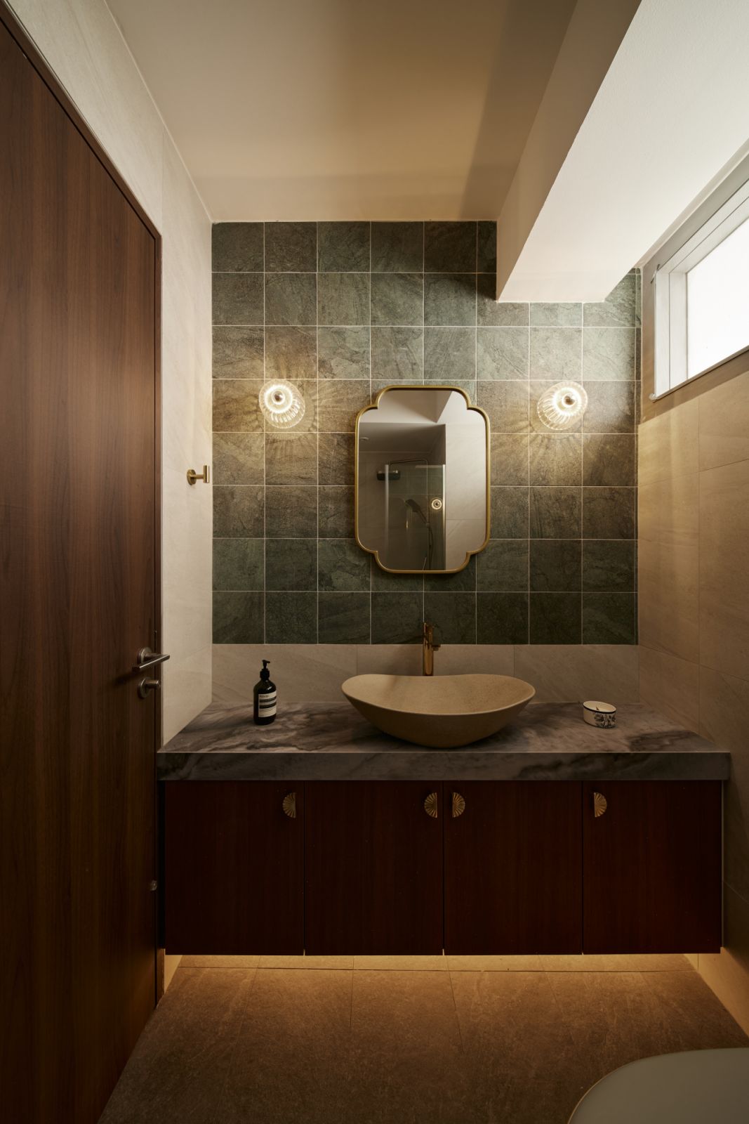 The powder room combines tonal richness with tactile materials—featuring a sculpted stone basin, brushed brass fittings and green slate tiles