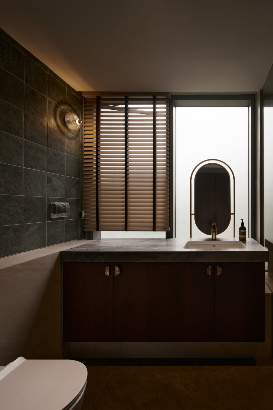 Seen at dusk, the bathroom is transformed by ambient lighting and layered materials, balancing privacy with a touch of quiet drama