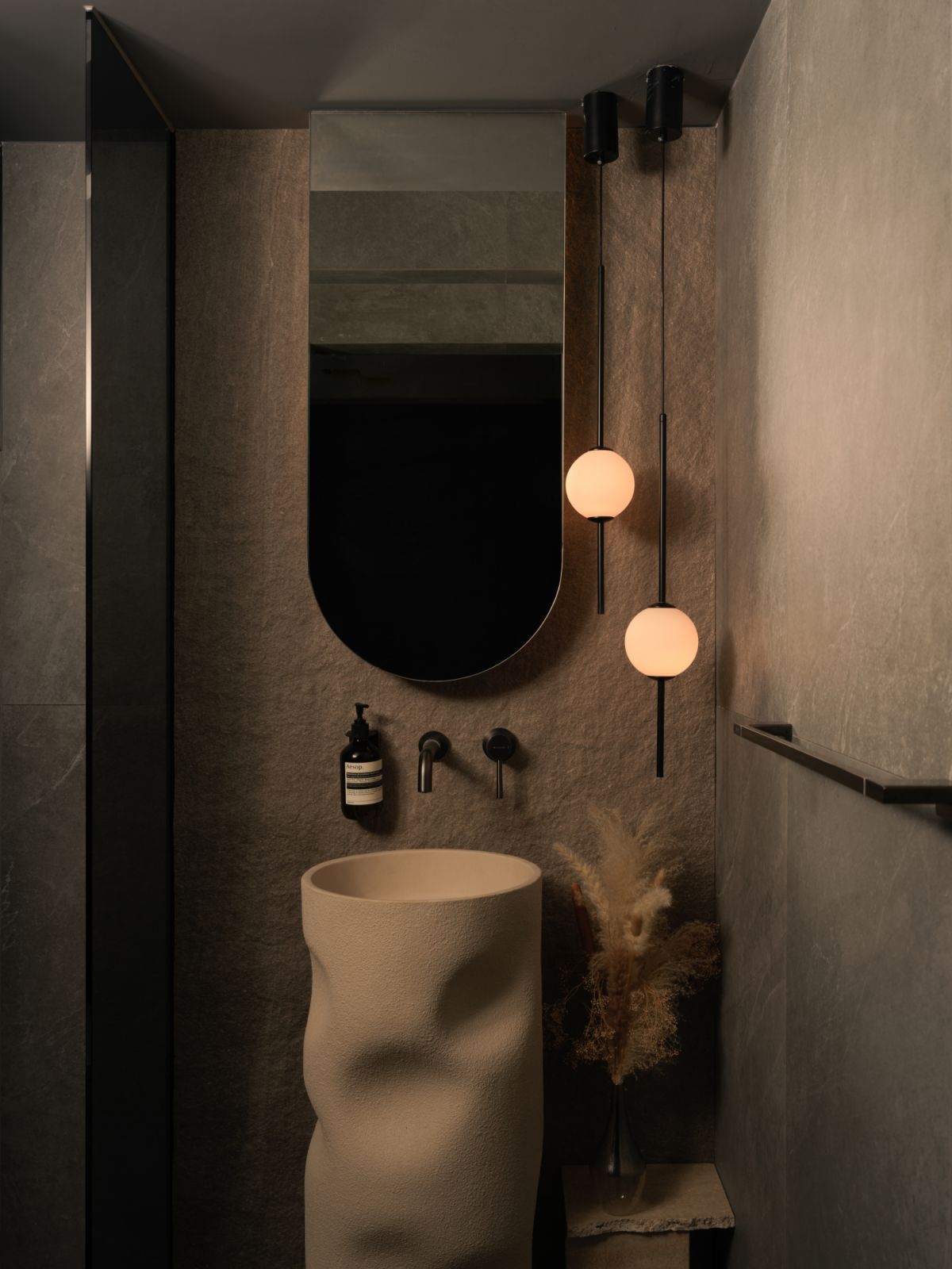 Textural drama takes centre stage in the powder room, where organic lighting meets a rippled pedestal basin set against earthy tiles