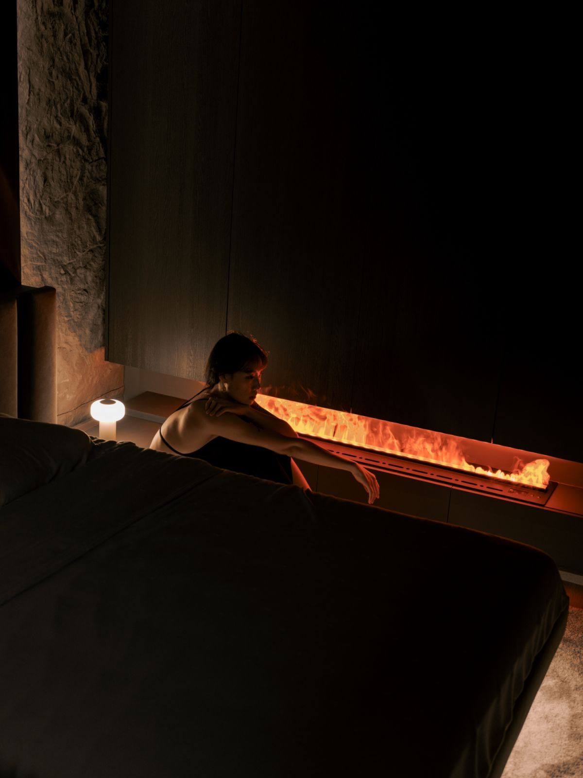 A glowing hearth sets the stage for quiet contemplation, its gentle flicker softening the sharp lines of the dark-hued bedroom