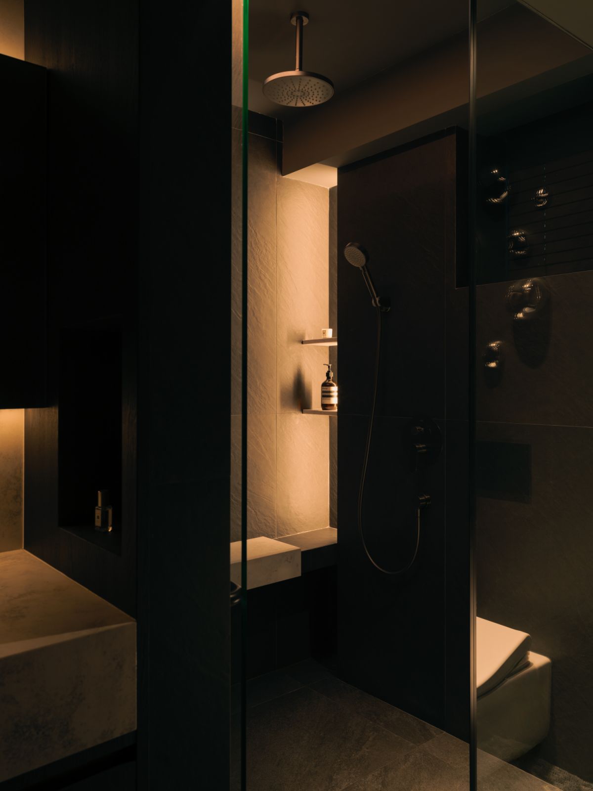 In the guest bathroom, tonal layers of stone and matte black fittings combine to create a refined spa-like sanctuary