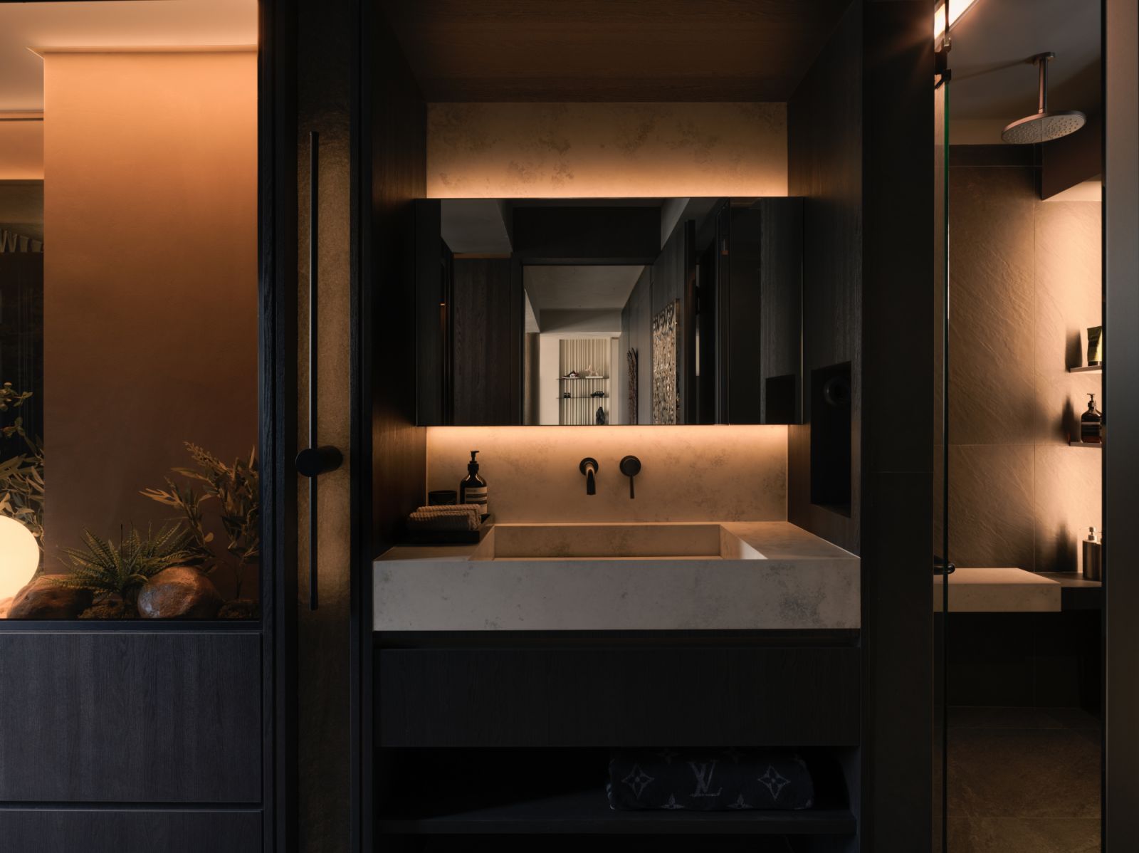 In the main ensuite, a stone-clad vanity with integrated lighting forms a sleek contrast against the dark timber surroundings