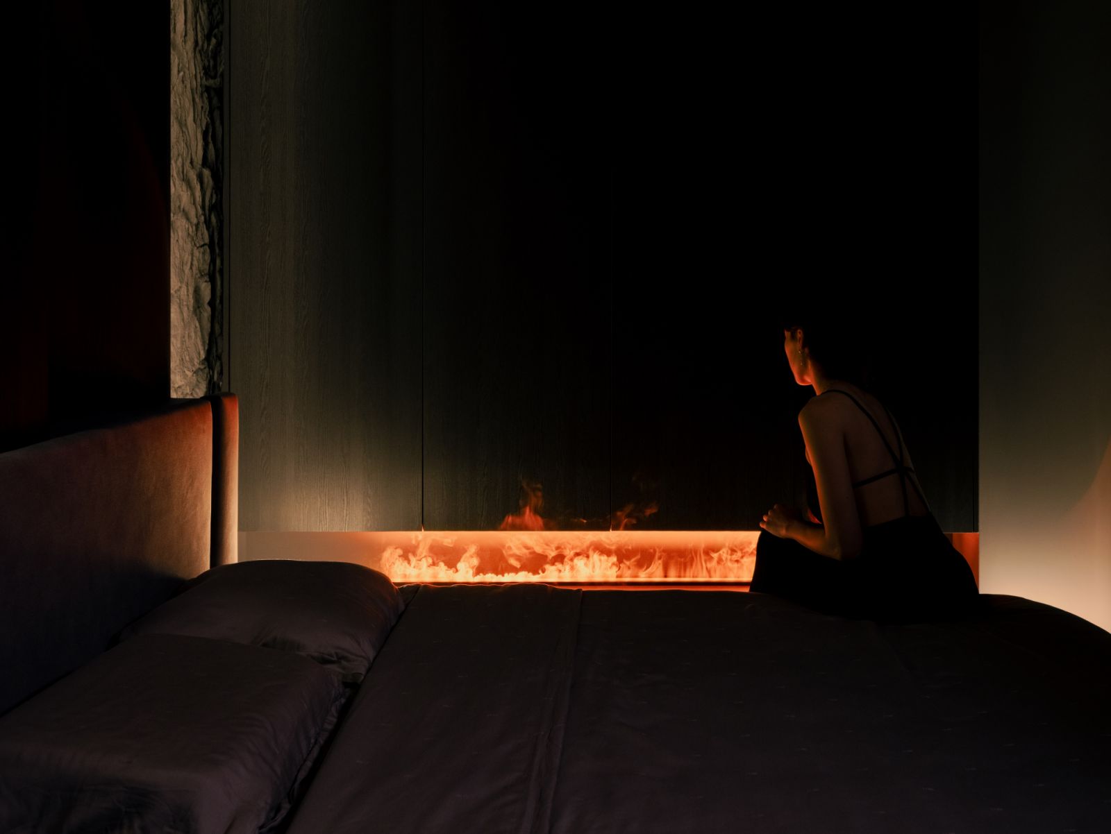 The bedroom takes on a moody, cocoon-like quality with a linear flame feature and textured backdrop enveloping the senses