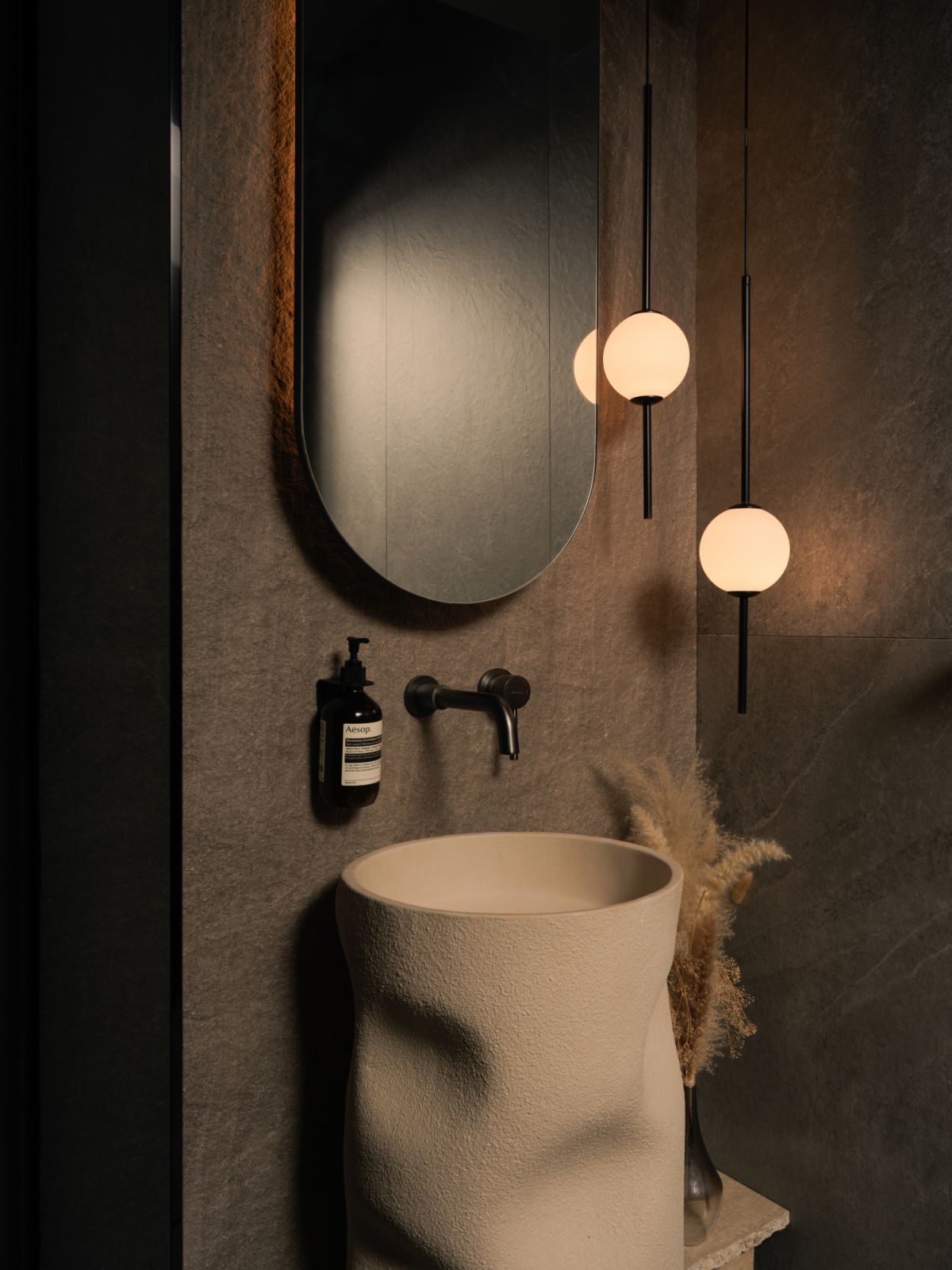 A sculptural sink with a textured, biomorphic form becomes the centrepiece of the powder room, paired with orb-like pendant lights that cast a gentle glow