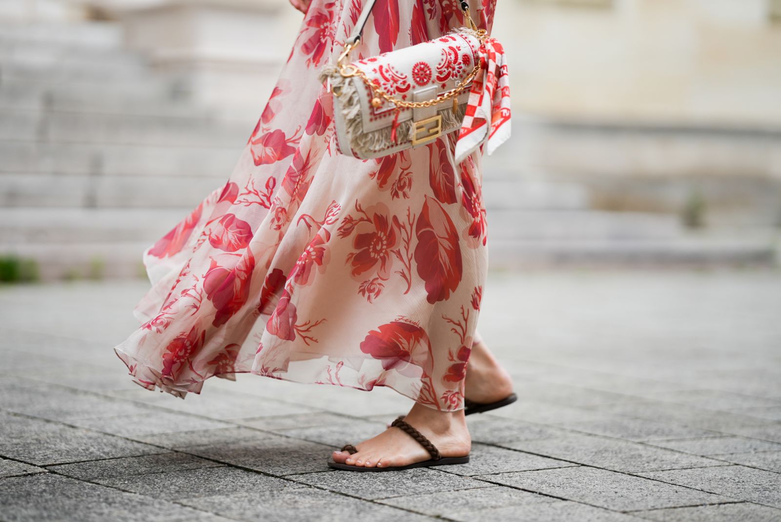MUNICH, GERMANY - MAY 29: Marlies Pia Pfeifhoher is seen wearing a light beige silk chiffon long sleeve maxi dress with red and pink prints of feathers and flowers, drawstring waist, deep V-neck with front tie and smocking details on the cuffs from FENDI, a natural-colored Baguette canvas bag with coral bandana embroidery, small fringes on the flap, calfskin leather straps, golden hardware and logo detail as well as an additional golden chain metal charm with marine-inspired pendants and a red, pink and whi