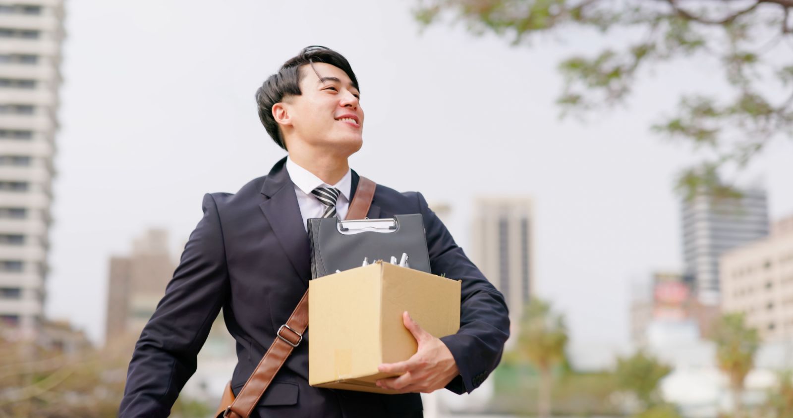 asian happy businessman quit his job and walk in city with box - fist gesture